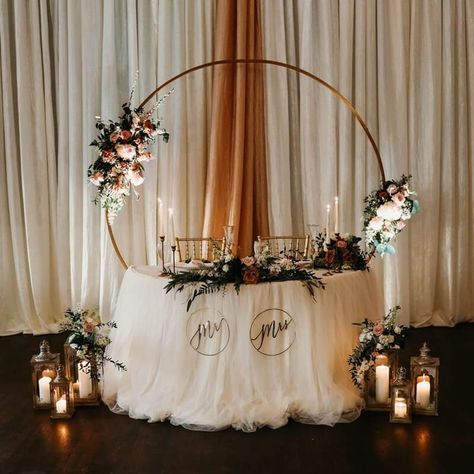 Dim the lights and keep the romance alive at your wedding head table by burning only wax taper candles in metal candle holders and wax pillar candles in metal patio lanterns. It is enough to reflect minimal light around you with white curtain panels to your table draped with white polyester tablecloth and tulle table skirt. Using silk rose bouquets and frosted faux plant, adorn your round backdrop frame and table. Ensure you have plastic wine glasses on hand for your first toast as newlyweds. Wedding Head Table, Event Decor Ideas, Party Decorations Table, Tulle Table Skirt, Patio Lanterns, Silk Rose Bouquet, Tulle Table, Wedding Arbors, Head Table Wedding