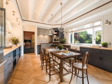 A spacious farmhouse table is the focal point of this dreamy cottage kitchen. Gray cabinets stretch across each side of the kitchen, providing plenty of storage space. The white vaulted ceiling and globe pendant lights add to the elegance. Galley Kitchen With Table, Kitchen With Table In Middle, Kitchen With Table, Kitchen Booths, Hgtv Kitchens, Kitchen Design Styles, Galley Kitchen Remodel, Small Kitchen Tables, Gray And White Kitchen