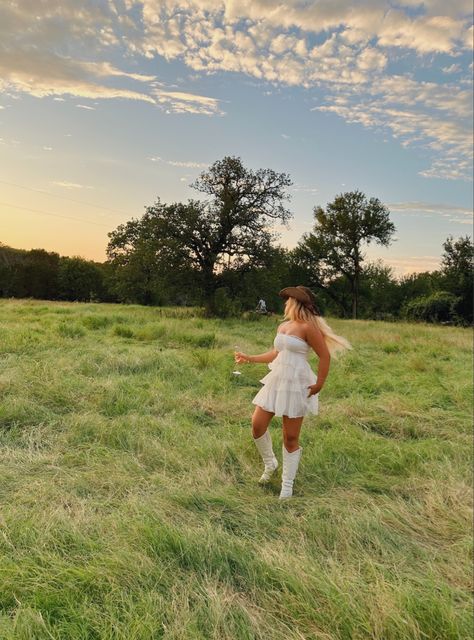 Feild , white dress , cowgirl boots , cowgirl hats , wine glass , flowy dress ,sunset girly Cowgirl Field Photoshoot, White Dress Cowgirl, White Dress Cowgirl Boots Outfit, Aesthetic White Dress, White Cowgirl Boots Outfit, Country Girl Dresses, White Cowgirl Boots, Foto Cowgirl, Tennessee Girls