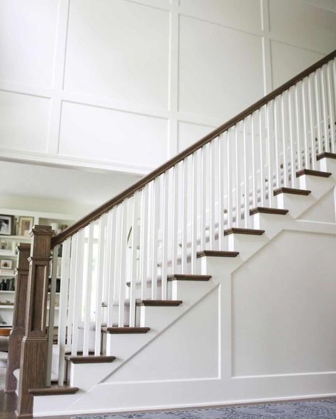 A glorious staircase leads up to the second floor of this lofty home, framed by wooden treads and a matching railing. The contrast between the wood and surrounding white walls is only enhanced by the board and batten wainscoting. Walls attached to high ceilings can sometimes seem a little bland, and adding texture is one way to remedy this...   Image: kitgoldeninteriors Board And Batten 2 Story Foyer, Staircase Paneling Ideas, Board And Batten Staircase, Full Wall Wainscoting, Wall Wainscoting Ideas, Stairs Wall Design, Modern Wainscoting Ideas, Board And Batten Wainscoting, Waynes Coating