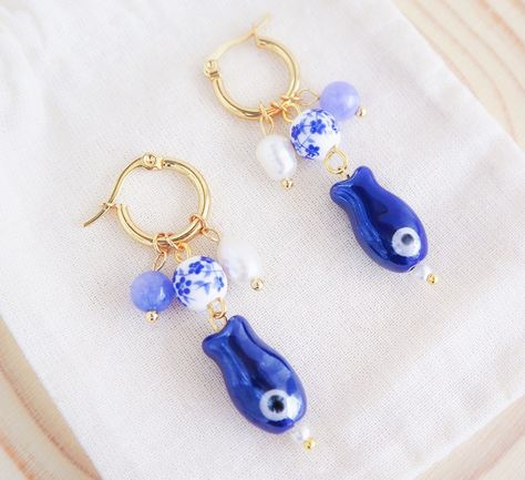 ༄ Handmade 𝙂𝙤𝙡𝙙 𝙎𝙖𝙧𝙙𝙞𝙣𝙚 𝘼𝙯𝙪𝙡𝙚𝙟𝙤 𝙋𝙚𝙖𝙧𝙡 earrings blend tradition with elegance. Inspired by the ocean and the historical culture of Portugal.🌊🐟🇵🇹 The dark blue ceramic 𝗦𝗮𝗿𝗱𝗶𝗻𝗲 𝗙𝗶𝘀𝗵 pendants honors Portugal’s coastal heritage and symbolizes resilience and prosperity.🐟 Combined with 𝗔𝗻𝗴𝗲𝗹𝗶𝘁𝗲 𝗴𝗲𝗺𝘀𝘁𝗼𝗻𝗲 beads, known for its calming properties, this bead reminds us of the calming ocean but also the colors of 𝗦𝗘𝗔 𝗕𝗬 𝗟𝗢𝗨.💙 The 𝗔𝘇𝘂𝗹𝗲𝗷𝗼 𝗧𝗶𝗹𝗲 ceramic bead inspired by Portugal’s iconic azulejos, these t... Sardine Fish, Ocean Inspired Jewelry, Seashell Earrings, Ocean Inspired, By The Ocean, Handmade Gold, Ocean Inspiration, Blue Ceramics, Inspired Jewelry