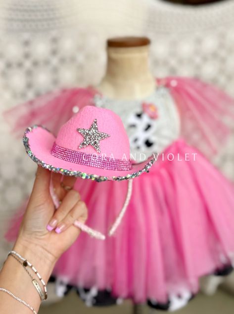 Good golly, let’s party like Dolly!  Pink and perfect,  this “just right” sized cowgirl hat has been decked out to be the perfect party accessory. Rhinestone-trimmed “belt” and rhinestone star perfectly accentuated by this hand-dipped rim in crushed holographic silver glitter and rhinestones.  Styled on a removable hea disco cowgirl hat headband Cora and Violet Disco Cowgirl Hat, Dolly Parton Birthday, Rodeo Party, Cowgirl Accessories, Cowgirl Birthday Party, Rodeo Birthday, Disco Cowgirl, Hat Headband, Happy First Birthday