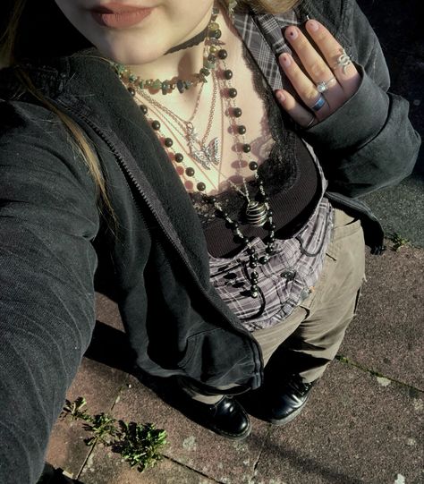 A mid-size person/girl wearing a thrifted tight grey waistcoat, a black lace tank top under it, wide dark olive green cargo pants, black platform dr. Martens and multiple crystal rings and bracelets. 	The person is also wearing multiple silver necklaces, one in form of a green crystal and another in form of a fairy  necklace, a black rosary-style bead necklace, a butterfly and a black lace choker. Grunge Green Pants Outfit, How To Style Green Cargo Pants Grunge, Fairygrunge Winter Outfits, Grunge Outfit Inspo Winter, Fairygrunge Aesthetic Outfits, Green Cargo Pants Outfit Grunge, Forest Style Clothes, Forest Punk Aesthetic Outfits, Mid Size Grunge Outfits