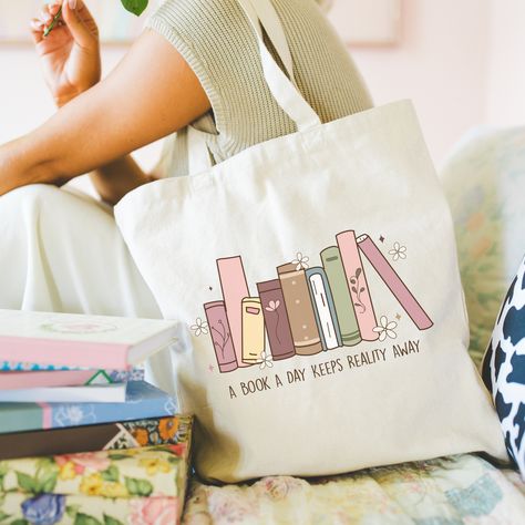 Indulge your bookish side with our charming Book Lover Tote Bag. Crafted from durable 100% off-white cotton canvas, this tote features a spacious, open design with a wide-mouthed opening for easy access to your essentials. The 1" cotton canvas handles are reinforced for added strength, ensuring comfortable carrying wherever your literary adventures take you. Design: Our Book Lover Tote Bag showcases a delightful book-themed design making it a stylish accessory for any bookworm. Whether you're heading to the library, bookstore, or simply running errands, let your love for literature shine with this eye-catching tote. Size: One Size - 16" tall x 15" wide Care Instructions: To keep your tote looking its best, spot wash with a warm soapy cloth and hang to dry. Please refrain from placing it in Bookish Tote Bag, Book Themed Gifts, Gifts Book, Library Bag, Best Tote Bags, Book Tote Bag, Girls Tote, Diy Tote Bag, Dream Gift