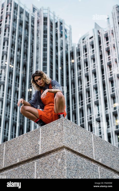 Download this stock image: Beautiful woman wearing dungarees, crouching on ledge in front of modern high-rise building - PG69DW from Alamy's library of millions of high resolution stock photos, illustrations and vectors. High Rise Building, Dynamic Poses, Dungarees, Beautiful Woman, Pose Reference, Print Images, Art Reference, Stock Images, High Rise