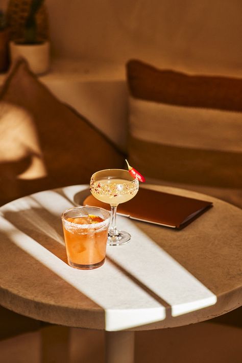 Cocktail photography of two margaritas upon a circular marble table in a Mexican themed bar. A short orange cocktail sits in a tumbler, with a salted rim. A chilli margarita in tall coup glass, decorated with salt, chilli flakes and a whole red chilli. Image belongs to Instant Crush Creative. Cocktail Photography Creative, Chilli Margarita, Mexican Interiors, Orange Cocktail, Orange Cocktails, Cocktail Photography, Drink Photography, Food Drink Photography, Hyatt Regency