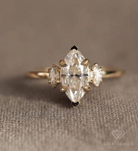 This stunning 14K yellow gold marquise cut moissanite wedding ring is a timeless treasure. Crafted with exquisite detail by skilled artisans, the 1.05-carat center stone boasts a brilliant, near-colorless sparkle.  Flanked by two smaller marquise cut moissanites, this three-stone ring symbolizes love, loyalty, and commitment. Moissanite, a brilliant alternative to diamond,  is known for its remarkable brilliance and fire.   Make this exquisite ring the perfect symbol of your love. Round Marquise Engagement Ring, Marquise 3 Stone Ring, Wedding Ring Stack Marquise, Marquis Moissanite Engagement Ring, Marquise Moissanite Ring, Vintage Marquise Engagement Ring Gold, Marquee Cut Engagement Ring, Marquee Wedding Ring, Marquise With Side Stones