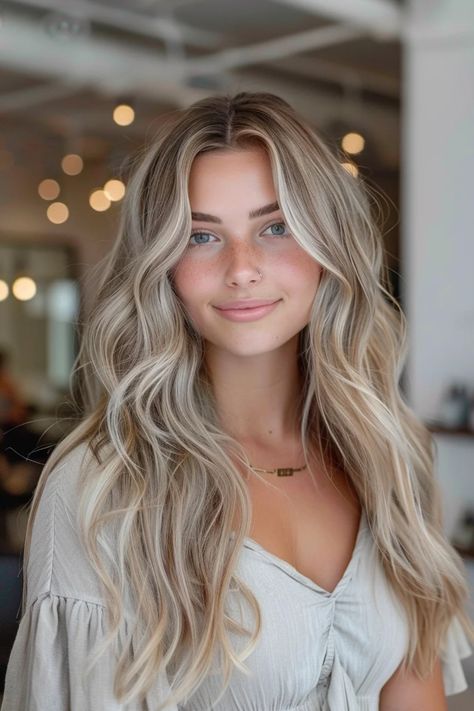 Woman with long blonde wavy hair and a necklace smiling indoors with blurred lights in the background. Blonde Balayage Light Skin, Light Blonde Hair With Brown Lowlights, Soft Summer Balayage, Blonde Hair Inspo Pics, Natural Blonde Hair Inspiration, Blonde And Dark Highlights, Hair Color For Cool Tone, Blonde Hair With Light Brown Lowlights, Dirty Blonde Hair With Layers