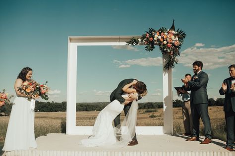 Jordyn and Kyle shared their first kiss under a sleek, contemporary white wedding arch adorned with an orange and pink corner floral arrangement. Wedding Arch Alternative, White Wedding Arch, Wedding Ceremony Arch, Unique Wedding Flowers, Wedding Ceremony Backdrop, Frame Wedding, Wedding Picture Frames, Ceremony Arch, Ceremony Backdrop