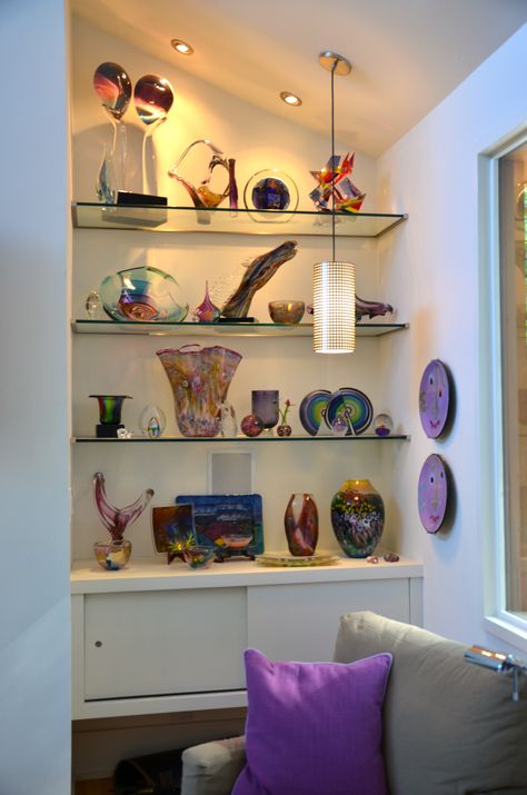 We created floating glass shelves in the niche beside a fireplace to showcase a client's glass art. The shelves are weighted at the bottom with a floating cabinet to house electronics and the space left underneath is perfect for a container of fire wood. Showpiece Shelves, Couch Shelf, Purse Closet, Above The Couch, Floating Cabinet, Glass Shelves Decor, Recessed Shelves, Shelves Decor, Floating Glass Shelves