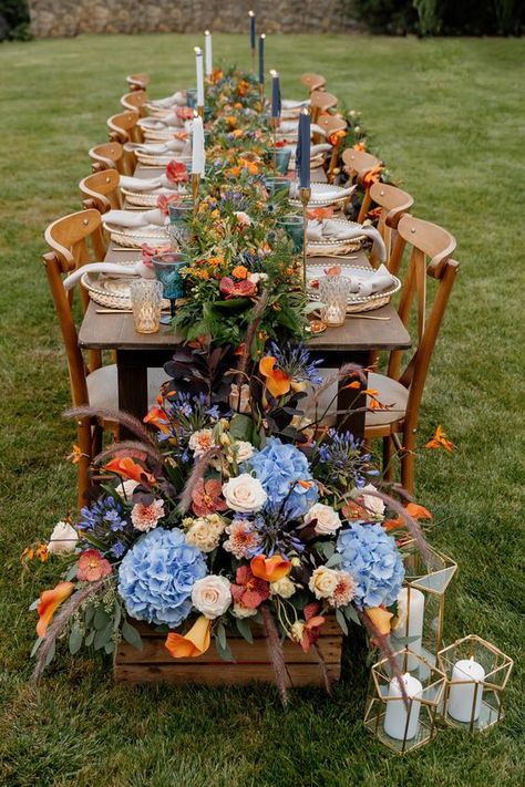 Cornflower blue and orange for fall wedding colors 2025, cornflower blue bridesmaid dresses, white bridal gown, navy blue groom suit, cornflower blue and orange flowers of boutonniere and centerpieces, white wedding cake with orange flowers décor. Orange And Blue Tablescape, Fall Wedding Color Schemes Blue, Blue And Orange Spring Wedding, Blue And Orange Wedding Centerpieces, Blue And Orange Fall Wedding, Blue And Orange Wedding Flowers, Wedding Cake With Orange Flowers, Cake With Orange Flowers, Orange And Blue Wedding Colors