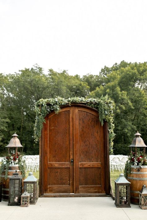 Enchanting outdoor wedding entrance to ceremony with beautiful fall florals and lanterns surrounding gorgeous wooden doors. Wedding Doors Outside Outdoor Ceremony, Outdoor Ceremony Entrance, Outdoor Ceremony Entrance Ideas, Wedding Door Entrance Outside, Outdoor Wedding With Doors Entrance, Wedding Outdoor Doors, Wedding Entrance Outdoor Ceremony, Wedding Ceremony Doors Entrance, Outside Wedding Doors Entrance