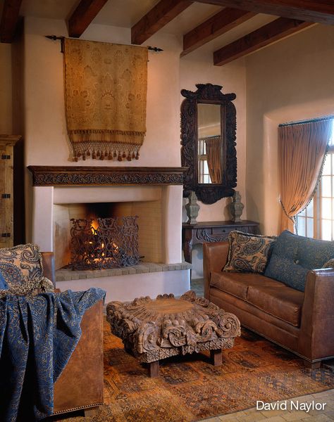 This Afghan Bhokara rug, in a rare shade of saffron, inspired the room. The coffee table is a repurposed column top. An embroidered French tapestry hangs above a fireplace shielded by an antique French screen. The mirror frame and mantel were carved in the Visions workshop. Santa Fe Interior Design, Santa Fe Interiors, Old World Interiors, Hacienda Homes, Interior Design Portfolios, Mediterranean Style Home, Living Room Family, Warm Interior, Old World Style