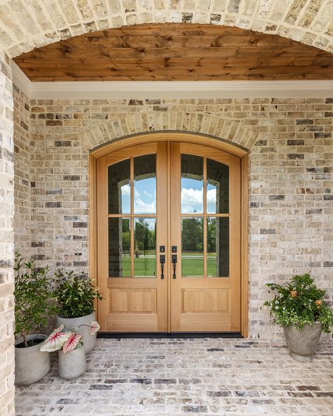 A grand entrance begins with a beautiful front door. This stunning arched double door, stained to match the rich wood ceiling of the front porch, sets the tone for the entire home. It’s the perfect blend of elegance and warmth, welcoming guests with style from the very first step. Arch Front Porch Entrance, Staircase By Front Door, Arched Front Doors, Arch Front Door Exterior Farmhouse, Front Doors Double, Double Exterior Doors, Round Double Door, Rounded Front Door Entrance, Grand Front Door