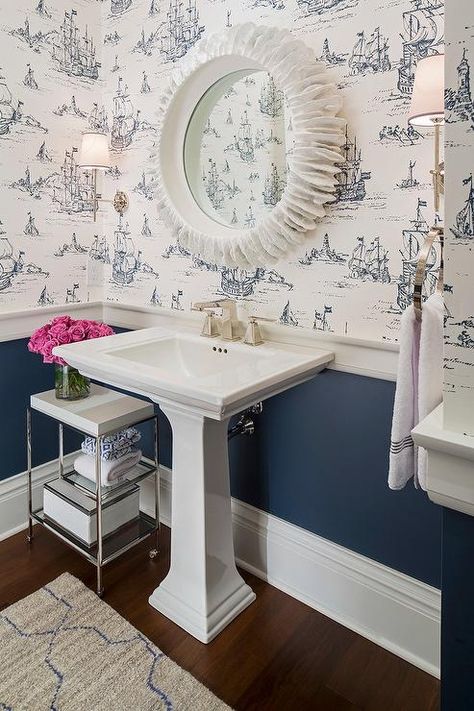 White and navy powder room features top half of walls clad in white and blue ship print wallpaper and lower half of walls painted navy blue finished with a thick chair rail. Navy Powder Room, Bathroom Wallpaper Nautical, Blue Powder Rooms, Chair Rail Molding, Powder Room Wallpaper, Classic White Kitchen, Pedestal Sink, Chair Rail, Trendy Bathroom