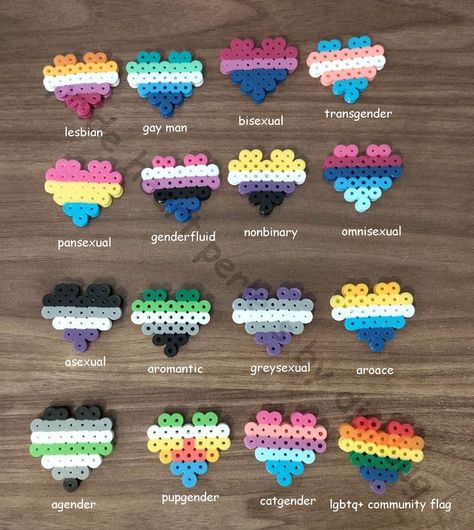 four by four rows of lgbtq+ flags made from perler beads in the shape of hearts on a wooden table as a background, from left to right these are the flags : lesbian, gay man, bisexual, transgender, pansexual, genderfluid, nonbinary, omnisexual, asexual, aromantic, greysexual, aroace, agender, pupgender, cat gender and the general lgbtq+ community flag. Cat Gender, Diy Kandi Bracelets, Hamma Beads Ideas, Easy Perler Bead Patterns, Pearl Beads Pattern, Easy Perler Beads Ideas, Perler Crafts, Diy Perler Bead Crafts, Kandi Patterns