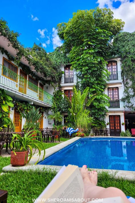 A woman sits poolside with a book in hand in the garden of Hotel Casa de la Tia Tere, Oaxaca City. Iron tables and chairs surround the blue pool and green plants and vines climb the outside of the hotel windows. Oaxaca Mexico Travel, Oaxaca City Mexico, Backpacking Spain, Mexico Itinerary, Spain Culture, Oaxaca City, Pool View, Mexico Travel Destinations, Wellness Hotel