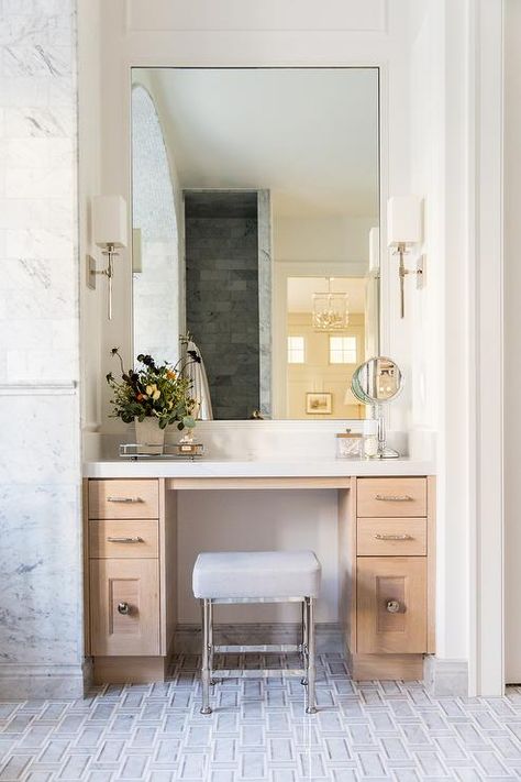 A gray leather seat sits on gray maze floor tiles at a blond wood makeup vanity adorned with polished nickel pulls and a white quartz countertop fixed beneath a tall mirror lit by Hudson Valley Lighting Taunton Wall Sconces. Vanity Nook, Vanity In Bathroom, Dressing Vanity, Wood Makeup Vanity, Makeup Vanity Decor, Design Hall, Marble Maze, Vanity With Mirror, Dressing Table Design