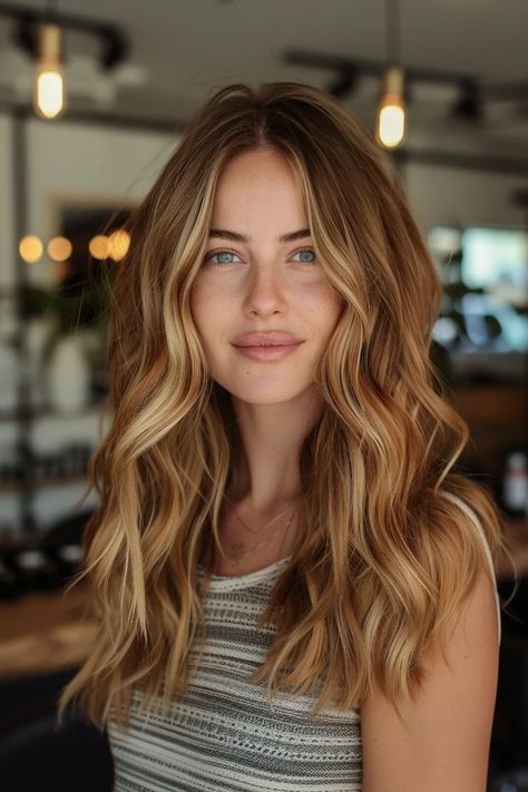 Woman with long wavy blonde hair and a striped top smiling indoors with blurred lights in the background. Cooper Blonde Balayage Brunettes, Toffee Blonde Hair Caramel, Butterscotch Blonde Hair Balayage, Balayage On Strawberry Blonde Hair, Gigi Hard Hair, Light Brown Hair With Caramel Balayage, Highlights For Ginger Hair, Fall Highlights For Light Brown Hair, Warm Hair Color Ideas Blonde