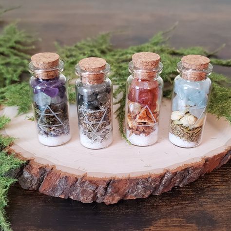 This 4 pack of elemental spell jars is potent but is also small enough to cast a spell or set up an altar anywhere! This set comes with all 4 elements- Air, Earth, Fire, and Water. Each 10mL bottle is smoke cleansed and filled with Sea Salt plus dried herbs and flowers such as Lavender, Peppermint, Sage, Mugwort, Cinnamon, Orange Peel, Thyme, and Jasmine. The bottle is also topped off with genuine crystals such as Fluorite, Amethyst, Pyrite, Smoky Quartz, Carnelian, Citrine, Moonstone, and Aquamarine. Each jar is labeled with the corresponding alchemical symbol and the jars are packaged together as a set making them perfect for gifting. How To Use: A Spell Jar is a powerful magickal tool that concentrates and amplifies the energies of the ingredients and intentions enclosed within it. Use Bottle Spells, Witchy Products, Yule Ideas, Magic Jar, Witch Bottle, Witches Jar, Spell Bottles, Spells Magic, Water Witch