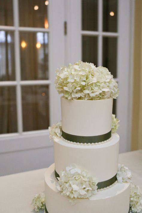 The ivory wedding cake had green ribbon wrapped around the base of each tier, and was accented with ivory hydrangeas. Wedding Cake With Hydrangeas And Roses, Cake Hydrangea, Hydrangea Wedding Cake, Wedding Cake Hydrangea, White Hydrangea Wedding, Hydrangea Cake, Cake Florals, Ivory Wedding Cake, Wedding Cake Pearls