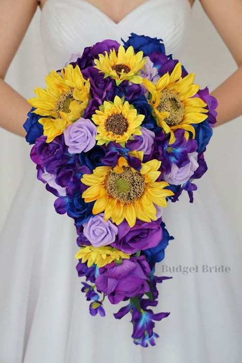 This lovely assortment of lavender, royal blue and purple roses is bound to turn heads on your wedding day. This lovely cascading brides’ bouquet from the is an absolutely breathtaking arrangement for any bride to be, in any season. Bright greenery, sunflowers and galaxy orchids complete the look and add a delicate realism to this beautiful bouquet. This bouquet is 10” wide, 18” long, and is crafted by our in-house florists without using a foam base to anchor the flowers to the bouquet. Instead, Violet And Blue Wedding Theme, Purple Teal And Sunflower Wedding, Purple Roses And Sunflowers Wedding, Purple Blue Sunflower Wedding, Purple Yellow And Blue Wedding, Royal Blue And Purple Wedding Ideas, Galaxy Wedding Bouquet, Blue Purple Yellow Wedding, Blue And Purple Fall Wedding