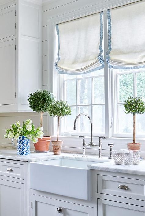 Windows dressed in white and blue roman shades are framed by a shiplap backsplash and positioned above an apron sink adorning a polished nickel deck mount gooseneck faucet fixed to a white marble countertop placed atop inset white shaker cabinets fitted with polished nickel cup pulls. Relaxed Roman Shade, Kitchen Window Treatments, Classic Kitchen, Roman Shade, Design Del Prodotto, Stylish Kitchen, Kitchen Window, Kitchen Curtains, Benjamin Moore