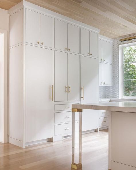 Brass and lucite legs, placed on gray wash wood floors under an oak plank ceiling, accent a white island topped with a gray and white marble countertop facing white concealed fridges placed both under and on either side of white flat front cabinets adorning Lewis Dolan Bar Pulls and Knobs. Kitchen Cabinets Pulls And Knobs, Cabinets Pulls And Knobs, Kitchen Cabinets Pulls, Flat Front Kitchen Cabinets, Flat Panel Kitchen Cabinets, Inset Kitchen Cabinets, Flat Front Cabinets, Flat Cabinets, Slab Cabinets