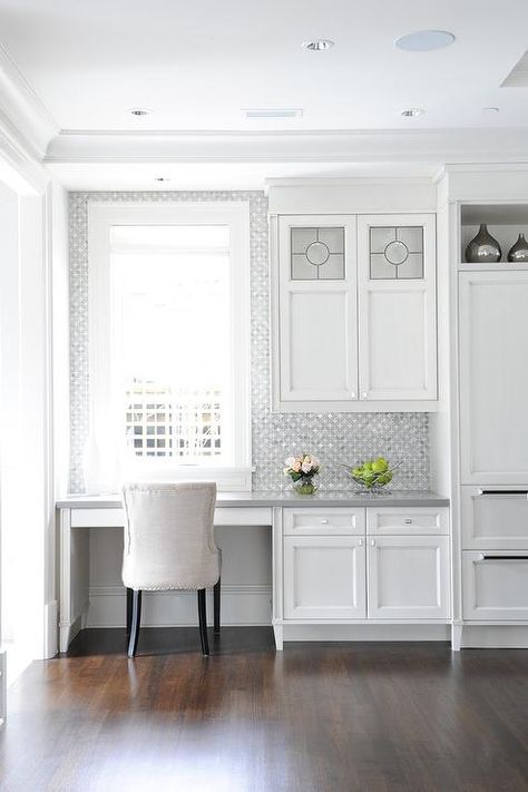 An ivory linen chair sits at a white built-in desk fixed in a kitchen and boasting a gray quartz top mounted beneath a window farmed by white and gray mosaic glass and porcelain tiles. Kitchen Office Nook, Studio In Casa, Kitchen Desk Areas, Kitchen Desks, Kitchen Desk, Home Office Inspiration, Office Nook, Study Nook, Desk Areas