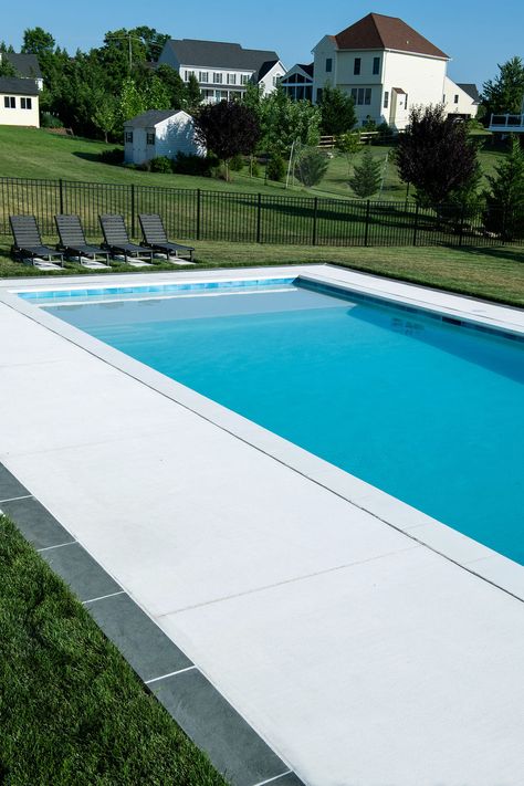 The white concrete pool deck shines bright in this clean, modern design. Pool Landscaping Concrete, White Concrete Pool Surround, White Concrete Pool Deck, Sand Finish Concrete Pool Deck, Pool Deck Concrete Ideas, Pool Concrete Colors, Pool Concrete Deck Ideas, White Concrete Pool, White Concrete Patio