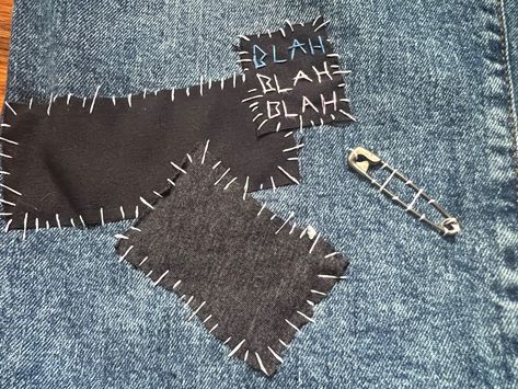 Black and grey fabric sewn onto blue jeans. A patch that reads blah blah blah written in blue, white, and pink is also sewn on. A safety pin is attached next to the 3 pieces of fabric. Punk Safety Pins Fashion, Pins On Pants, Sewn On Patches, What To Do With Safety Pins, Diy Punk Jeans, Patch Jeans Punk, Safety Pin Outfits, Punk Pins Diy, Punk Crafts Diy