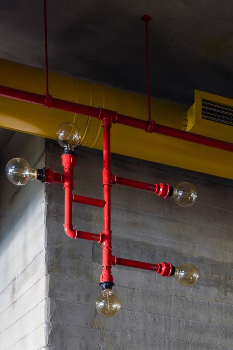 Crat Bar interior design by Lera Bykova. The main light in the whole space is designed from the water pipes that are painted in red. Textured concrete walls. The exposed duct system in yellow color. Yellow Industrial Interior, Pipe Lighting Ceiling, Exposed Electrical, Pipes Design, Industrial Bar Design, Black Pipe Lights, Industrial Lamp Design, Industrial Pipes Factory, Interior Design Industrial