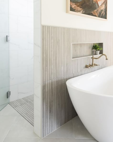 Vintage brass faucet is mounted to a gray vertical skinny tile tub surround over a white freestanding tub. The tub stands on gray tile bathroom flooring next to a white and gray marble tile shower. Beige Shower Tile, Gray Tile Bathroom, Kenridge Ribbon, Hexagon Tile Bathroom Floor, White Subway Tile Shower, Gray Shower Tile, Tile Tub, Marble Shower Tile, Tile Tub Surround