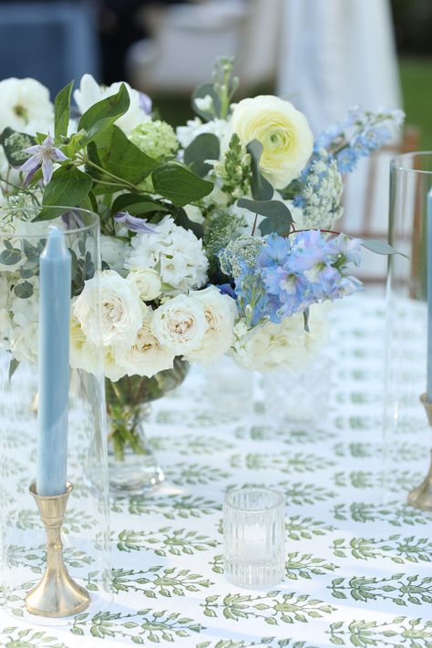 a green and white patterned table linen. the floral arrangement has white and blue flowers with greenery. Green And Blue Tablescape, Green Wedding Linens, Blue And White Tablescapes Wedding, Blue Table Linens Wedding, Blue Green And White Wedding, White Green And Blue Wedding, Wedding With Blue Accents, Blue Green Wedding Colors, Coastal Centerpiece Ideas