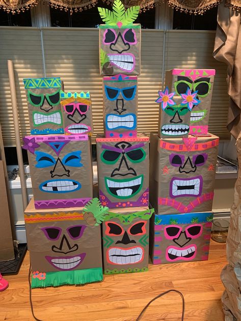 Homemade tiki heads made from assorted cardboard boxes, wrapped in brown craft paper, and decorated with fluorescent card stock paper. Tiki Mask Box, Diy Tiki Mask Cardboard, Tiki Costume Diy, Tiki Heads Diy Boxes, Cardboard Tiki Totem, Tiki Theme Party Decorations, Diy Cardboard Surfboard, Hawaiian Float Ideas, Tiki Totem Diy