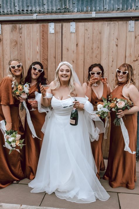 Bride in off the shoulder wedding dress with bottle of champagne standing with the bridal party in burnt orange satin bridesmaid dresses with white heart retro sunglasses | bridal party | bridesmaid dress inspiration | Lucy Alexandra Photography Bridesmaid Dresses With Bride, Orange Satin Bridesmaid Dresses, Bridal Party Sunglasses, Bridesmaid Dress Inspiration, Blue Bridesmaid Dresses Short, Bridesmaid Dresses Indian, Heart Retro, Off The Shoulder Wedding Dress, Indian Bridesmaid Dresses