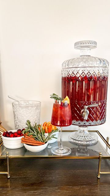 Samantha Bauchmann on Instagram: "LARGE BATCH HOLIDAY RUM PUNCH // the perfect addition to any holiday/christmas/New Years party you’re throwing in the next few weeks! INGREDIENTS: 72 oz 100% cranberry juice 24 oz orange juice 24 oz apple cider 24 oz orange liquor 36 oz spiced rum Garnishes - cranberries, orange slices, cinnamon sticks, rosemary springs INSTRUCTIONS: 1) combine cranberry juice, orange juice, apple cider, orange liquor and spiced rum in large drink dispenser (mine holds 200 oz). Add cranberries, orange slices and cinnamon sticks to top for garnish. 2) Setting up station, add small bowls of garnishes + bowl for ice. Fill wine glass with ice, add punch and garnishes. Serve and enjoy! #cocktails #holidayparty #hosting #easyrecipe" Drink Dispenser Cocktails, Christmas Drink Dispenser, Large Drink Dispenser, Holiday Rum Punch, Samantha Bauchmann, Sangria Drink, Christmas Party Drinks, Christmas Sangria, Orange Liquor