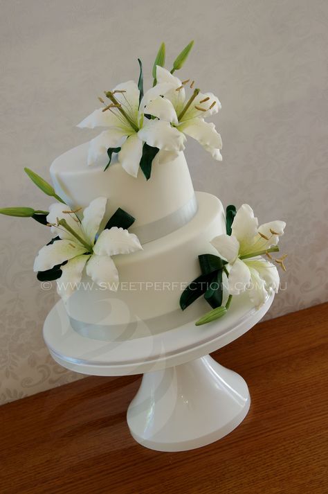 Two-tiered white wedding cake, with sugar bridal lilies and silver organza ribbon. Venue:Redhead Beach SLSC. Lily Wedding Cake, Cake Quinceanera, Calla Lily Wedding Cake, 40 Cake, Lily Cake, 25th Wedding Anniversary Party, Red Birthday Cakes, Wedding Cake Images, Round Wedding Cakes