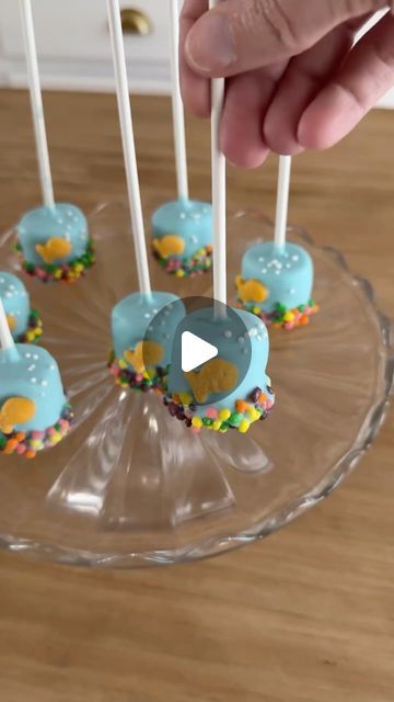 Sheri Wilson on Instagram: "Fish Bowl Marshmallow Pops! 🐠 the perfect treat for a pool party and so easy to make! This is a fun activity the kids can join in with as well! 

Ingredients:
Large marshmallows 
Blue chocolate wafers, melted
Nerds candies
Goldfish crackers
White sprinkles
Lollipop sticks

1. Dip the end of a lollipop stick into the melted chocolate, then press into the marshmallows.
2. Dunk each marshmallow into the melted chocolate and allow the excess chocolate to drip off.
3. Dip the bottom of each marshmallow in Nerds candies for the “pebbles”, then add a goldfish cracker and sprinkles for the bubbles.

#cakepops #marshmallow #easyrecipes #poolparty #summerrecipes #summerfood #summerdessert" Marshmallow Skewers, Sheri Wilson, Large Marshmallows, Dolphin Party, Marshmallow Sticks, Marshmallow Dip, Nerds Candy, Goldfish Crackers, Marshmallow Pops