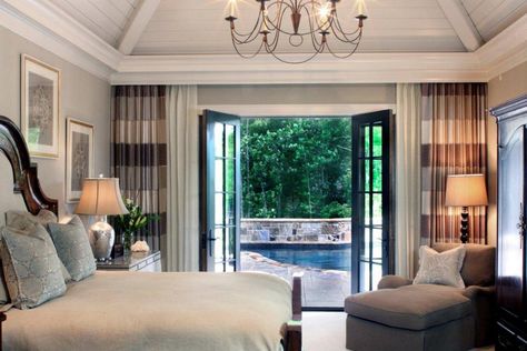 This transitional master bedroom features French doors that open to the pool, which create a private resort-like feel. Wall-to-wall curtains add texture and interest as well as draw the eye to the doors and out onto the patio. Vaulted ceilings and a stunning chandelier add drama and height to this cozy space. Bedroom Patio Doors, Bedroom French Doors, Master Suite Addition, French Doors Bedroom, Bedroom Addition, French Doors Exterior, Storage Inspiration, Neutral Bedrooms, Bedroom Patio