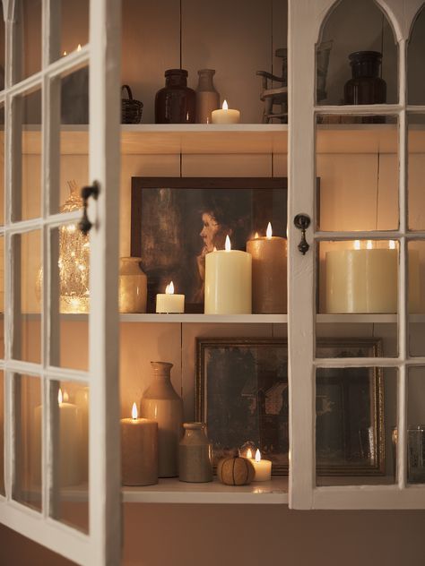 Cabinet filled with photos, vases and varying LED candles. Autumn Candles, Dining Centerpiece, Indoor Lanterns, Ivory Candles, Cosy Autumn, Orange Candle, Autumn Candle, Pumpkin Lights, Fall Candles