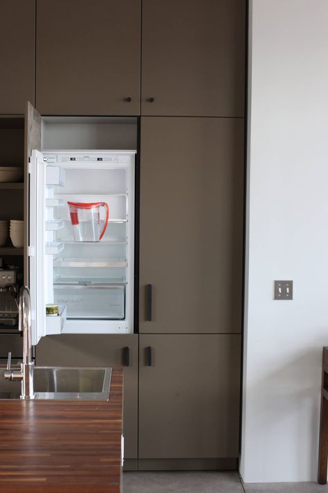 A Bosch 24-inch refrigerator is hidden in a system of cabinets with a custom panel front. Clients can choose to integrate the refrigerator into a tall freestanding piece of furniture or nest it within cabinets as shown. “When clients want a larger refrigerator, I recommend using two side-by-side like a French door setup,” Karcher says. Refrigerator Nook, Refrigerator Cabinet Ideas, Refrigerator Enclosure, Hidden Refrigerator, Refrigerator Cabinets, Hidden Fridge, Modern Refrigerator, Alcove Ideas, Panel Ready Refrigerator