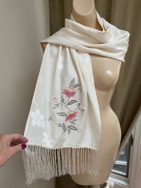 "Lovely embossed silk scarf/wrap in an ivory color with a flower embossed finish.   56\" length and 14\" wide - length doesn't include the 5\" silky fringe on either end.   I don't think this is long enough to wear as a shoulder wrap but more like a scarf as I've shown in the pictures. Pale cream beige color with a tiny sheen.   A large embroidered vine of flowers in shades of antique rose and sage on one end and a tiny single flower on the other end. Two layers of silk so no threads from the em Traditional Embroidered Cream Scarf, Elegant Embroidered Cream Scarves, Elegant Embroidered Silk Shawl Scarf, Elegant Beige Embroidered Scarves, Elegant Cream Embroidered Scarf, Embroidery Scarf, Silk Scarf Wrap, Embroidered Scarf, Fringe Scarf