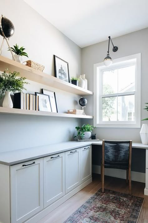 Blond wooden shelves are styled and stacked over a built-in l-shaped desk boasting white shaker cabinets and a gray desk top seating a black rope chair. Coastal Home Office, Best Benjamin Moore Paint Colors, Coastal Office, Working Room, Modern Coastal Home, Benjamin Moore Paint Colors, House Move, Home Bunch, Modern Farmhouse Home