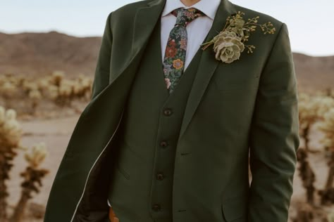 Close up photo of groom's green suit, floral tie and succulent boutonnière. Evergreen Suit Wedding, Eclectic Groom Attire, Fall Wedding Tux Groom Attire Green, Men’s Garden Wedding Attire, Earthy Groom Attire, Desert Wedding Groom Attire, Bridesman Outfits Green, Green And Brown Groom Suit, Unique Suits For Men Wedding