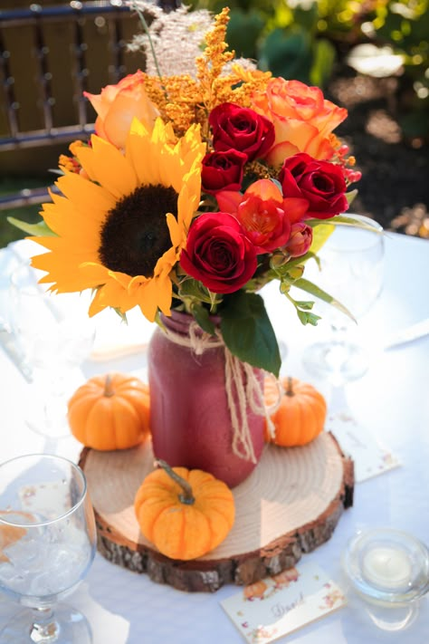 These outdoor fall wedding reception centerpieces included bright sunflowers, red roses, and other seasonal flowers alongside mini pumpkins and rustic wood pieces. This photo was taken by Megan Leigh Photography at one of our real fall weddings located at @josephamblerinn. Fall Wedding Centerpieces Sunflowers, Fall Wedding Decor With Sunflowers, Fall Bridal Centerpieces, October Wedding Sunflowers, Sunflower And Rose Centerpieces Diy, Pumpkin Sunflower Centerpiece, Fall Centerpiece With Sunflowers, Sunflower Red Rose Wedding Decor, Fall Centerpieces Wedding Pumpkin