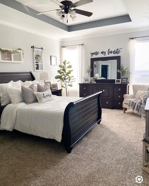 A dark wood sleigh bed is pushed against light grey bedroom walls. The bed is made with a white bedspread while a variety of beige and white pillows are placed at the head. An off-white armchair sits in the corner on the beige carpet. Bedroom Inspirations Dark Furniture, Dark Wood Bedroom Furniture, Light Gray Bedroom, Dark Wood Bedroom, Dark Brown Furniture, Brown Furniture Bedroom, Dark Bedroom Furniture, White Wall Bedroom, Dark Wood Furniture