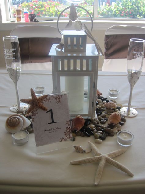 Bride and Groom Table. This time they use a white lantern with seashells for a beach theme. Nautical Lantern Centerpiece, Wedding Shower Tables, Rehearsal Dinner Centerpieces, Beach Table Decorations, Barbados Wedding, Beach Centerpieces, Lantern Decor Wedding, Grooms Table, Lighthouse Crafts