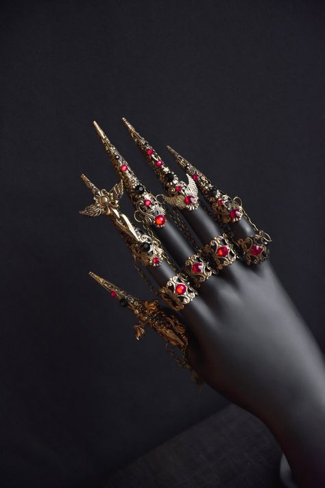 Beautiful gothic claw rings will be a great addition to your look. The photo shows a set of claws and medium rings in old gold color. The claws are decorated with small swords with wings and black and red rhinestones. The middle rings are attached to the claws with small chains.  The set includes 5 long claws and 4 medium rings Suitable for small and medium fingers. Not suitable for very wide fingers Claw rinds is available in different colors (see last photo). Finger Chain Ring, Red And Gold Accessories, Finger Claw Jewelry, Finger Claws, Hand Armor, Claw Rings, Brass Knuckle, Full Finger Rings, Claw Ring