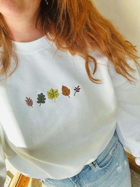 Introducing our Autumn Leaves Embroidered Sweatshirt, the perfect addition to your fall wardrobe. This 2D Crewneck Sweatshirt is not only stylish but also a thoughtful gift for your loved ones. With its exquisite embroidery and cozy design, it effortlessly combines fashion and comfort. Our sweatshirt features a stunning autumn leaves design meticulously embroidered on the front, showcasing the beauty of nature in its vibrant colors. The intricate detailing and precise stitching make this sweatsh Cozy Sweatshirt Aesthetic, Embroidery Ideas Machine, Fall Embroidery Designs Sweatshirt, Cute Fall Sweatshirts, Embroidered Gifts Ideas, Hand Embroidery Sweatshirt, Fall Leaves Embroidery, Trendy Embroidery Designs, Happy List